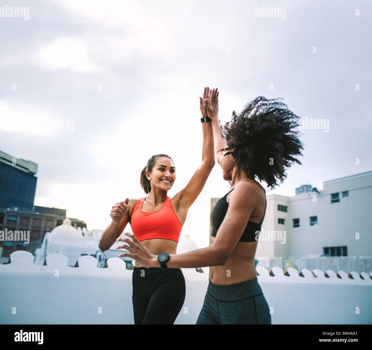 Zwei fröhliche Frauen in der Eignung für hohe fünf während der Ausführung auf der Terrasse. Frauen Athleten zu tun Fitness Training auf dem Dach hohe Fiv Stockfoto