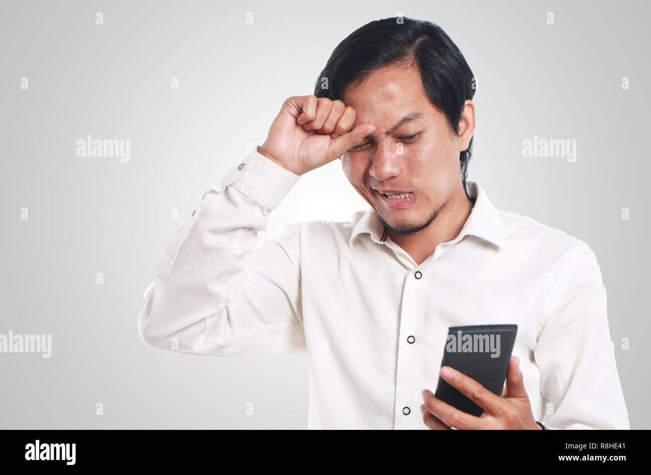 Foto Portrait eines lustigen jungen asiatischen Mann entsetzt, während Sie schlechte Nachrichten auf seinem Smartphone. Schlagen Kopf Halten Sie mit einer Hand das Telefon mit anderen h Stockfoto