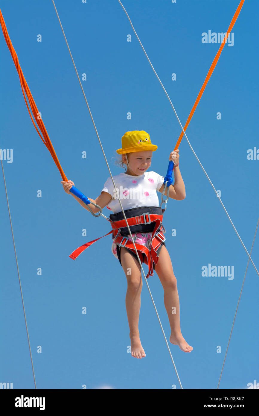 Ein kleines Mädchen springt auf einem Trampolin mit Gummiseilen gegen den  blauen Himmel und weißen Wolken. Abenteuer- und Extremsport. Konzept der  Sommer Vac Stockfotografie - Alamy