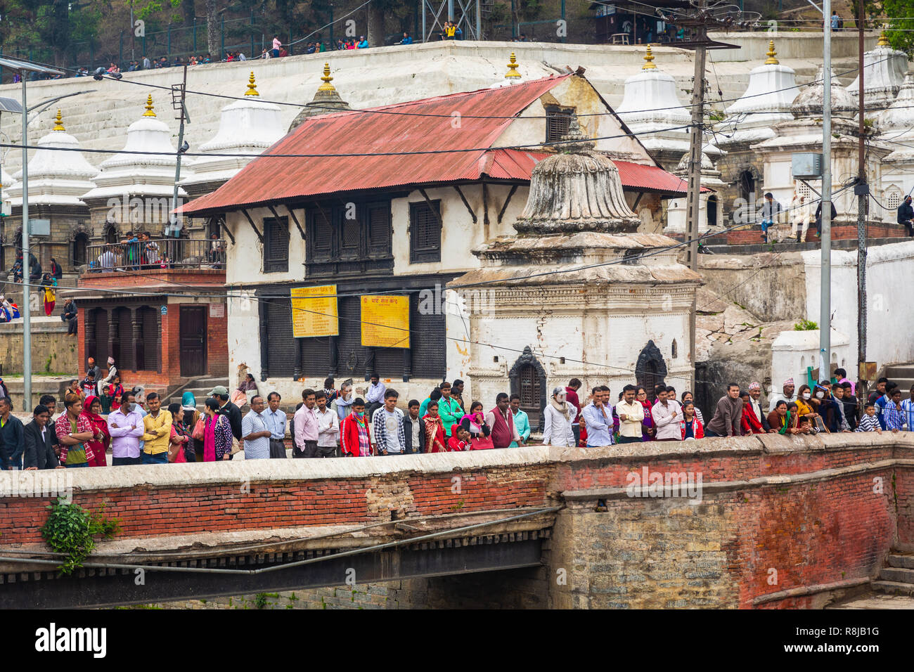 Menschen auf der Brücke beobachten ein Hindu Beerdigung auf der Ghat auf den Bagmati River am Heiligen hinduistischen Pashupatinath Tempel in Kathmandu, Nepal Stockfoto
