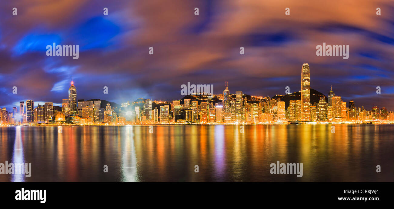Unscharfe schnell Wolken über Hong Kong City CBD Hochhaustürmen dart bei Sonnenaufgang, wenn helle Beleuchtung von Bürogebäuden reflektiert in Gewässern der Victo Stockfoto