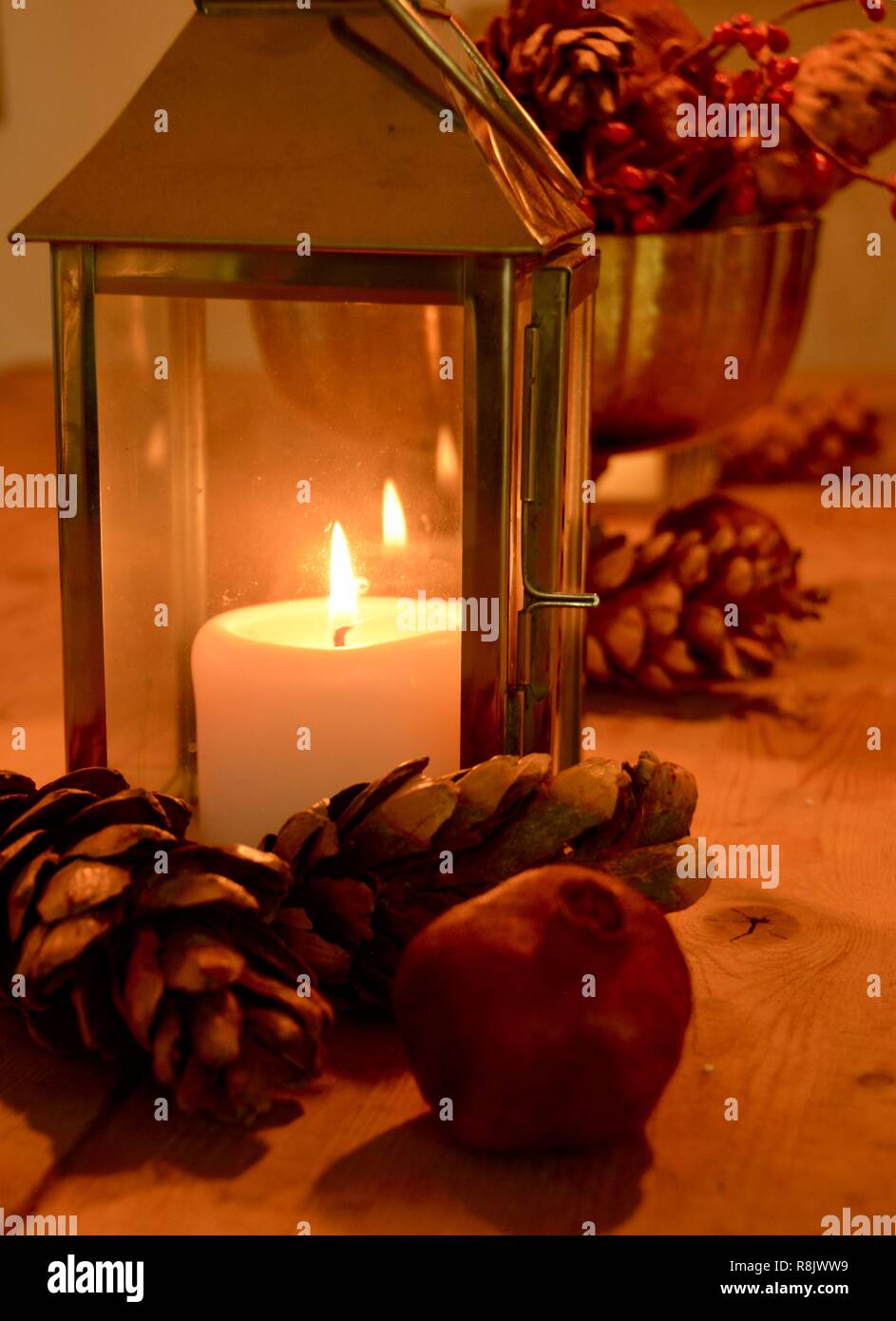 Weihnachten Tischdekoration mit einem glühenden Kerzenlicht, kiefernzapfen und ein Granatapfel. Stockfoto