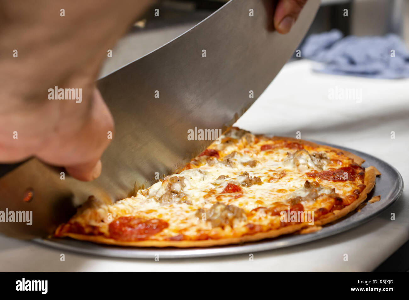 Koch Schneiden eine Pizza mit einem mezzaluna in einem Restaurant. Nahaufnahme von der Seite. Hände nur sichtbar. Stockfoto