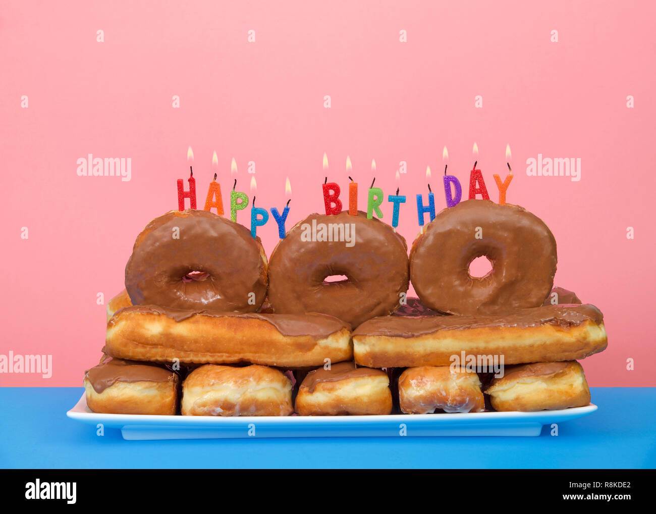 Schokolade Donuts auf einer rechteckigen Platte mit Happy Birthday Kerzen  brennen auf der Oberseite, blau Tisch rosa Hintergrund gestapelt. Donut  Liebhaber Geburtstag Stockfotografie - Alamy