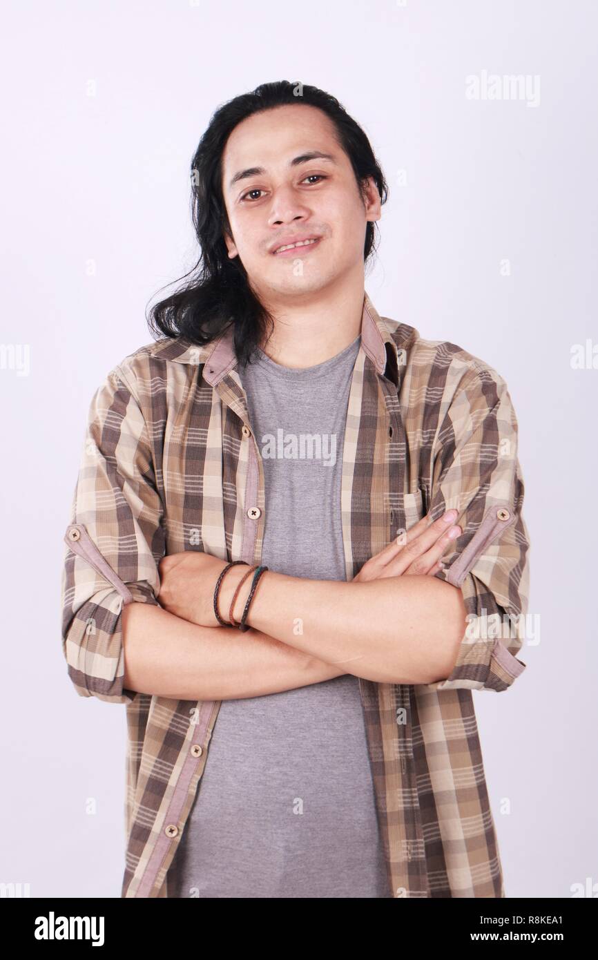 Foto Portrait von eine nette junge erfolgreiche asiatische männliche Kursteilnehmer mit langen Haaren, lächelnd und stand mit verschränkten Armen vor der Brust gekreuzt Stockfoto