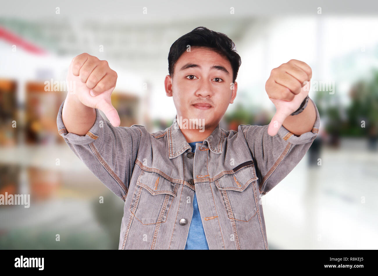 Foto Portrait von eine nette junge asiatischer Mann tun spöttische Geste und zeigt zwei Daumen nach unten Stockfoto
