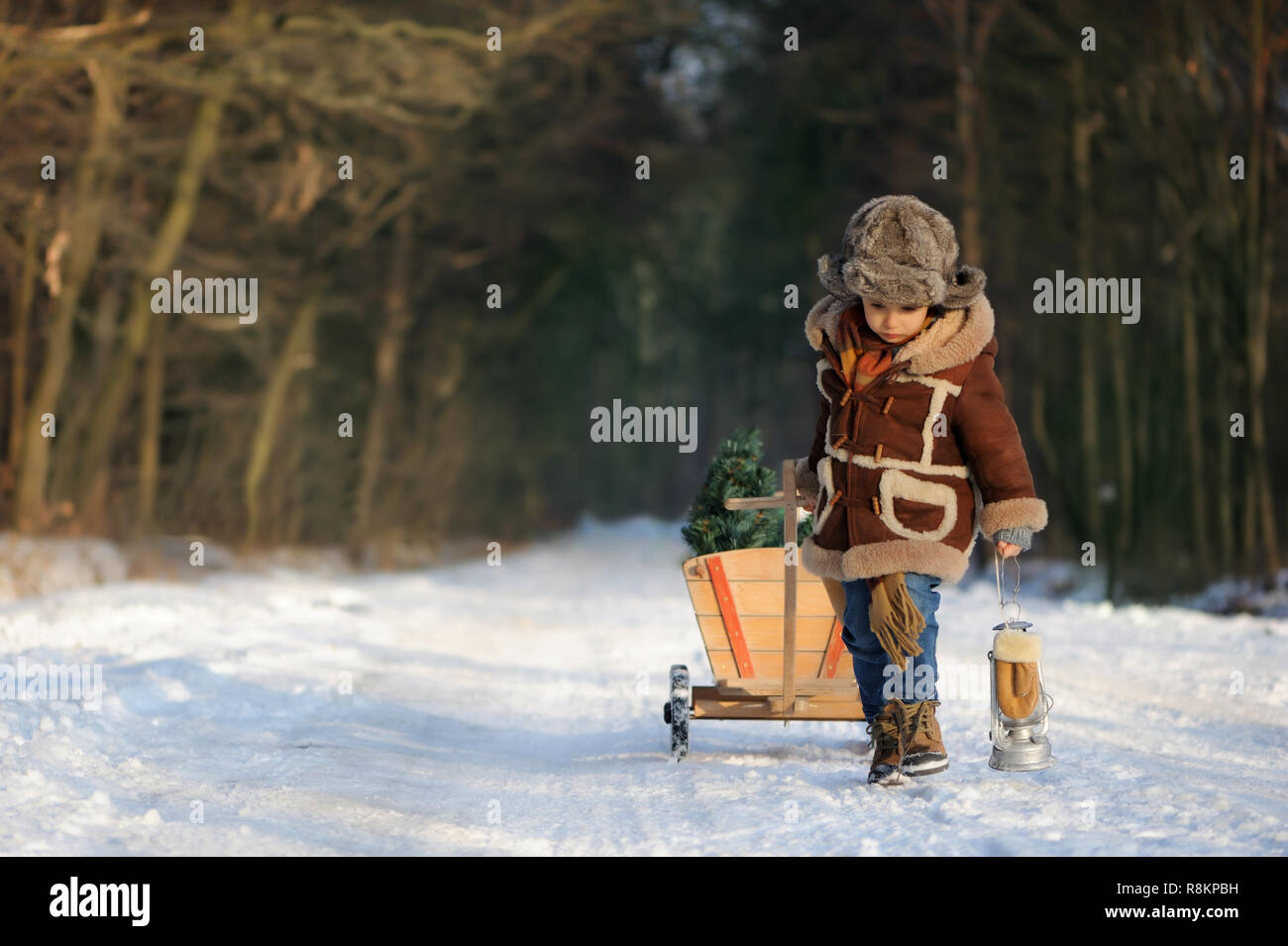 Junge mit einem Weihnachtsbaum im Wald. Winter Portrait of a Boy im Freien in einem braunen Schaffellmantel und Fell hat, in einer verschneiten Landschaft. Schön, kalt Stockfoto