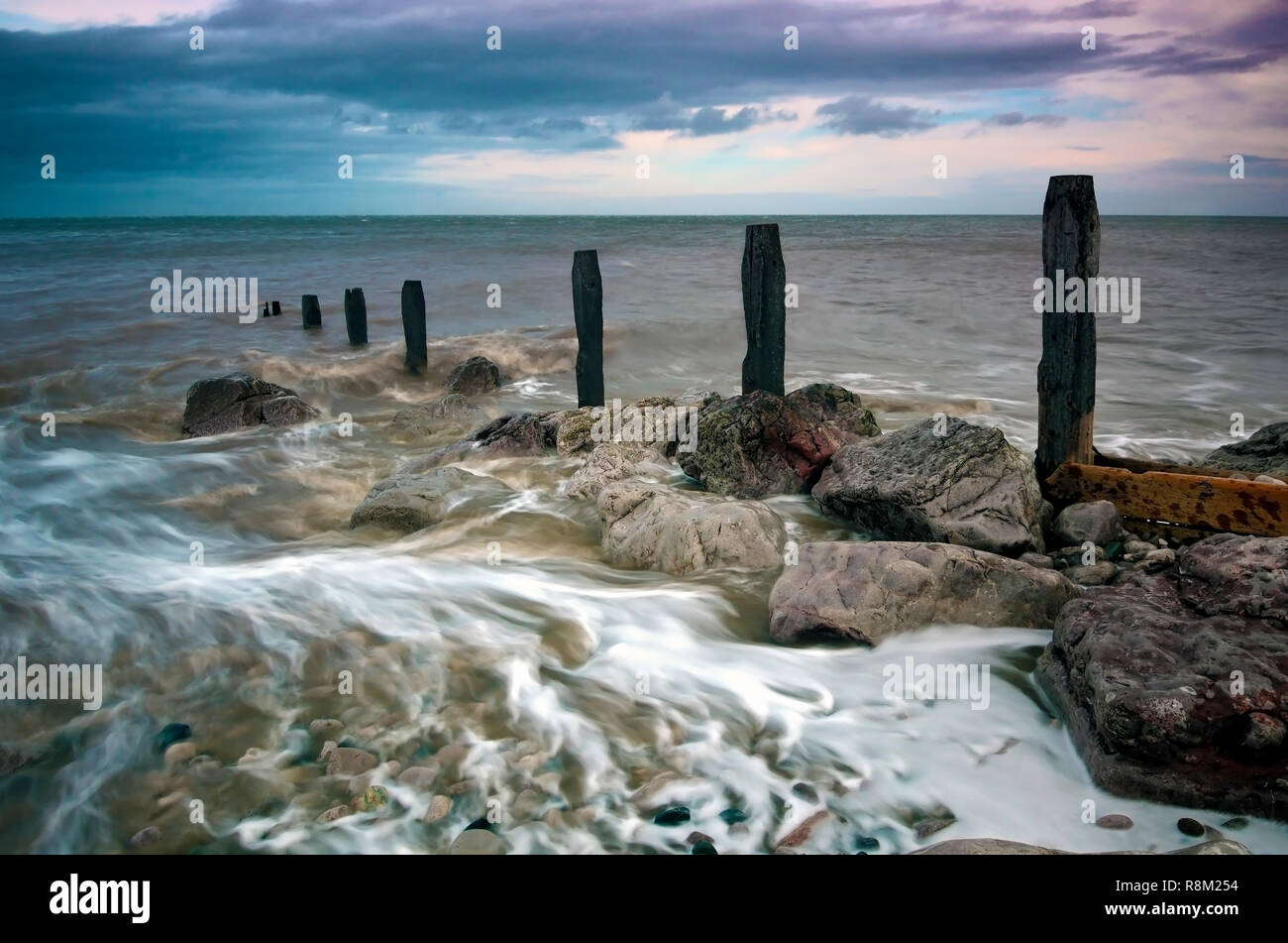 Wasser fließt über die Reste der Buhnen entlang der Kiesstrand in Llanddulas, North Wales. Stockfoto