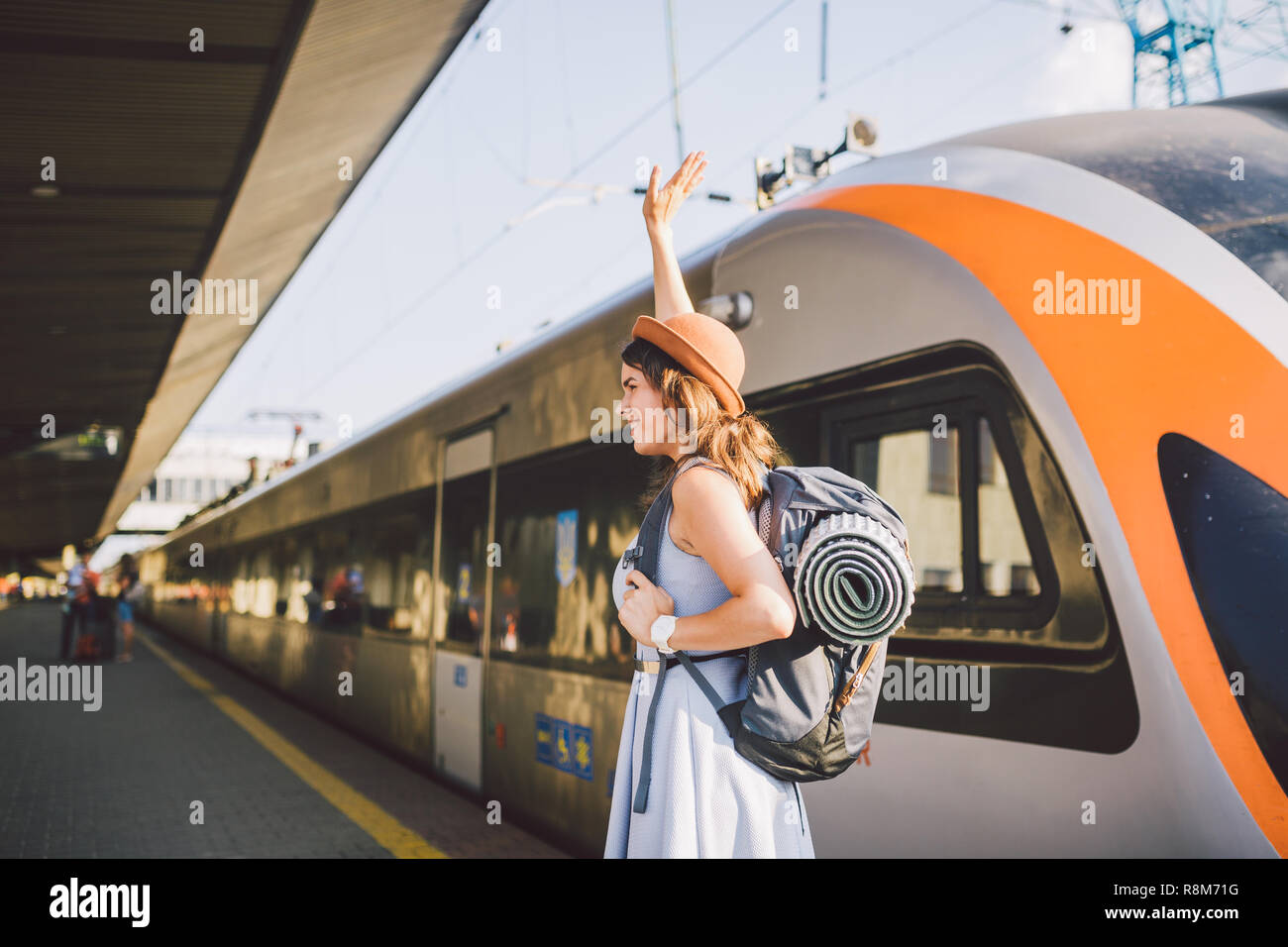 Thema Transport und Reisen. Porträt der jungen kaukasischen Frau mit toothy Lächeln am Bahnhof Hintergrund mit Rucksack winken Hallo w Stockfoto
