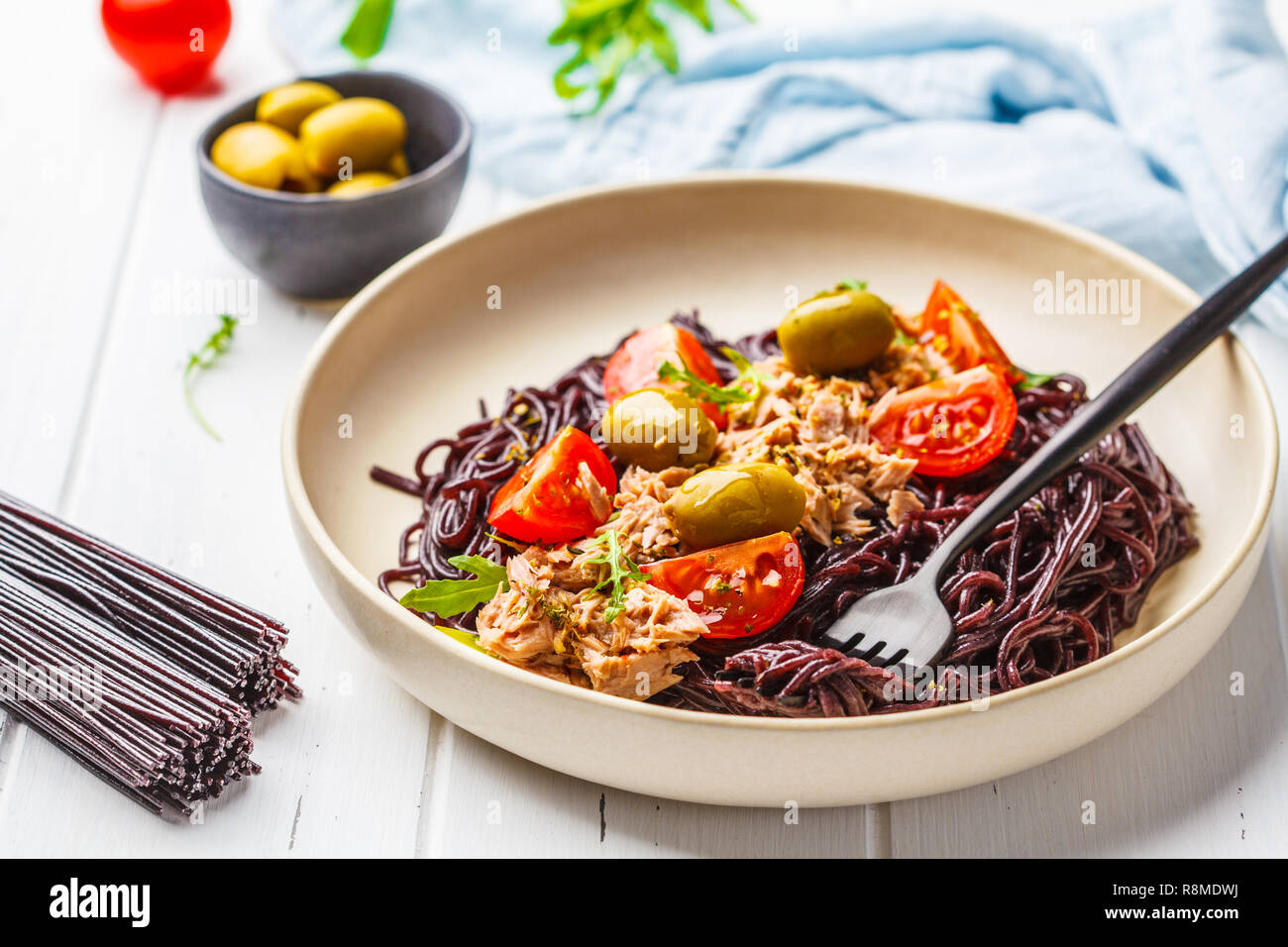 Schwarzer Reis Nudeln mit Thunfisch, Tomaten und Oliven in eine weiße Platte auf weißem Holz- Hintergrund. Stockfoto