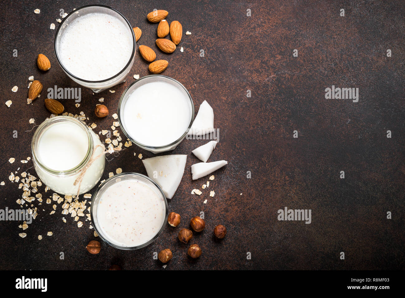 Vegan ohne Milchprodukte alternative Milch. Kokos-, Mandel-, Haselnuss-, Hafer hausgemachte Milch mit Zutaten. Dunklen Stein Tabelle Ansicht von oben. Stockfoto