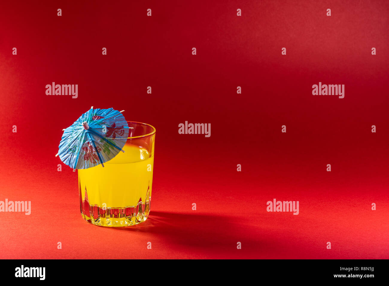 Orange Drink auf rotem Hintergrund mit Regenschirm. Weiches Obst Drink mit einem Cocktail Regenschirm. Stockfoto