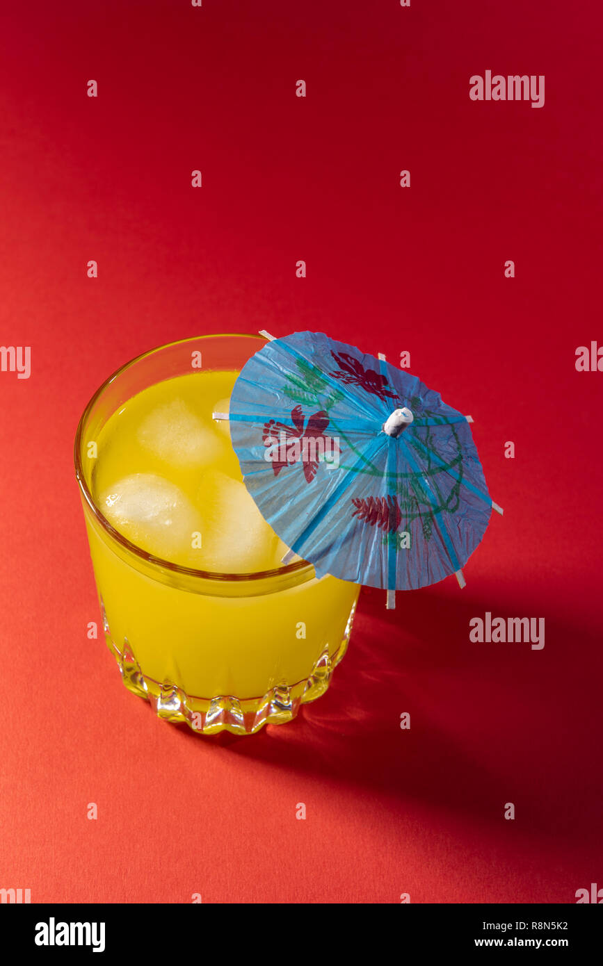 Orange Drink auf rotem Hintergrund mit Regenschirm. Weiches Obst Drink mit einem Cocktail Regenschirm. Stockfoto