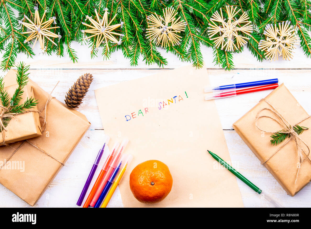 Auf dem hölzernen Tisch sind ein altes gelbes Papier, das sagt, Lieber Weihnachtsmann rot, Bleistifte, Kugelschreiber versch. Farben Geschenk und Zweige für das neue Jahr Stockfoto