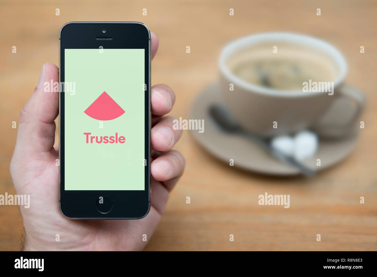 Ein Mann schaut auf seinem iPhone die zeigt die Trussle Logo (nur redaktionelle Nutzung). Stockfoto