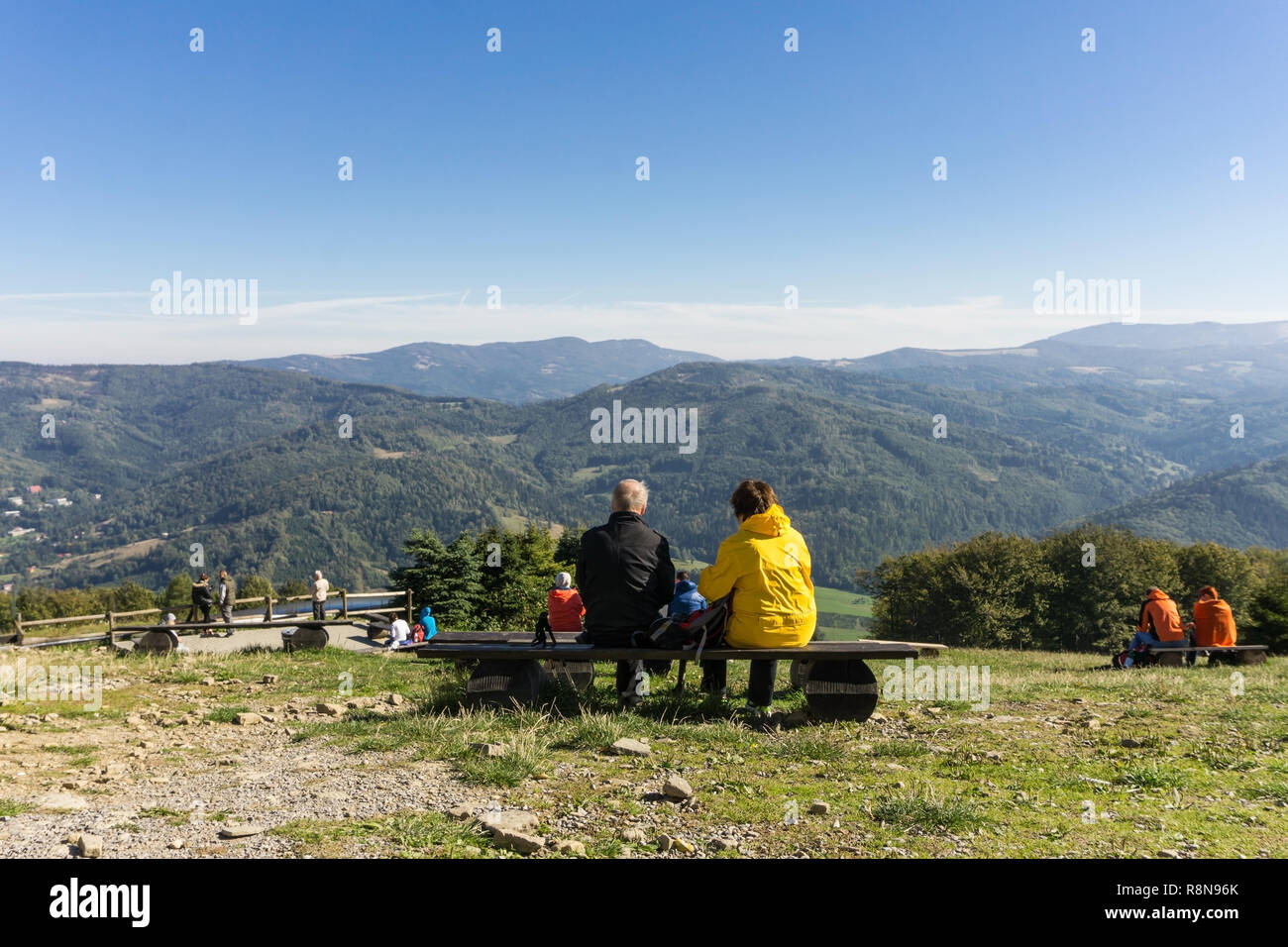 Reifes Paar ruht auf einer Bank in den Bergen an einem sonnigen Tag - Rückansicht - schöne Berglandschaft Stockfoto