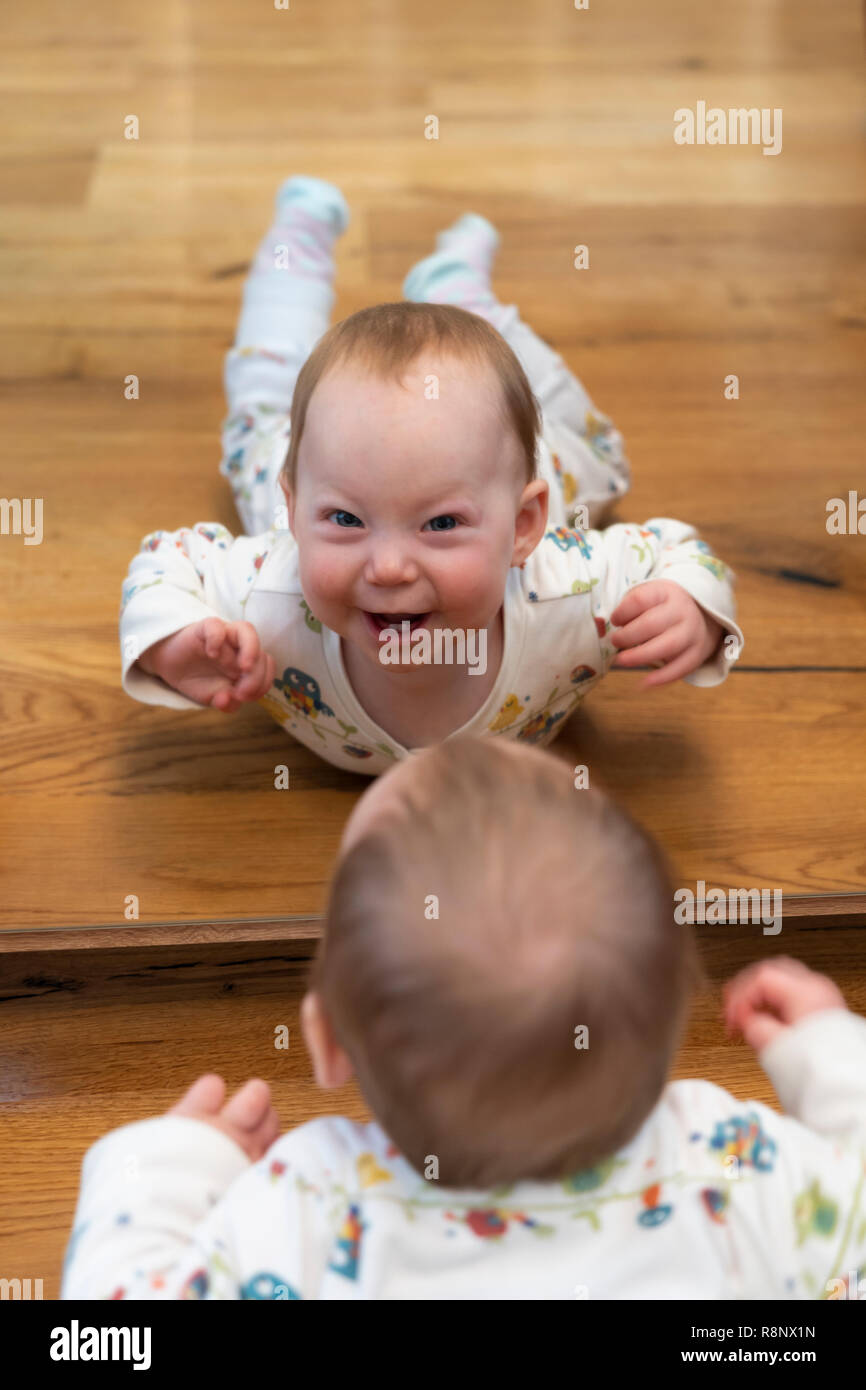 Die Reflexion eines neun Monate alten Baby Mädchen schauen in den Spiegel und lächeln auf den Betrachter Stockfoto