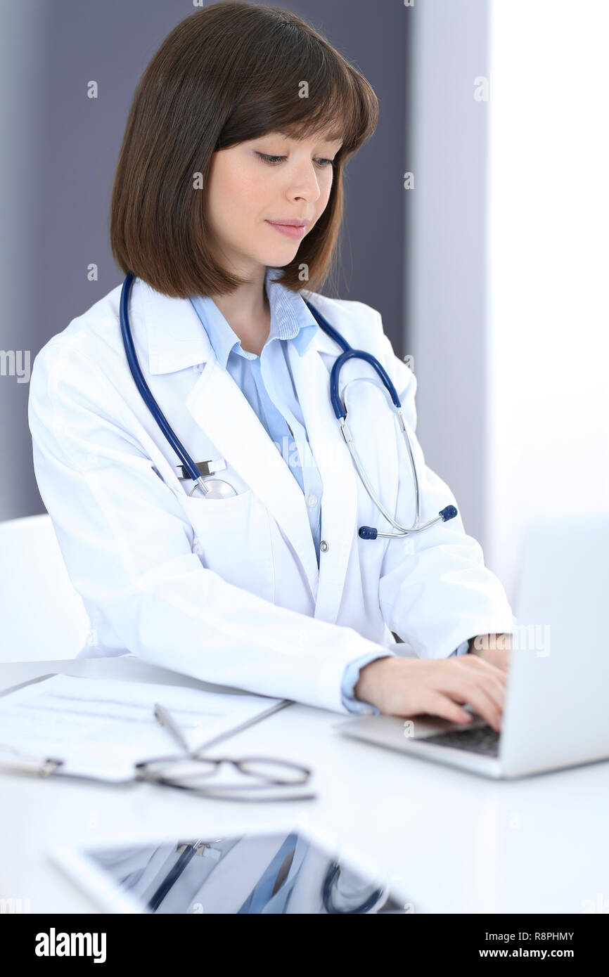 Arzt tippt auf Laptop beim Sitzen am weißen Tisch im Krankenhaus. Arzt bei der Arbeit. Medizin und Gesundheit Konzept Stockfoto