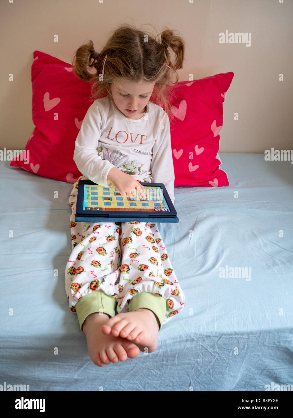 Vier Jahre altes Kind ein Spiel spielen auf einem Tablett in ihrem Schlafzimmer, Großbritannien Stockfoto