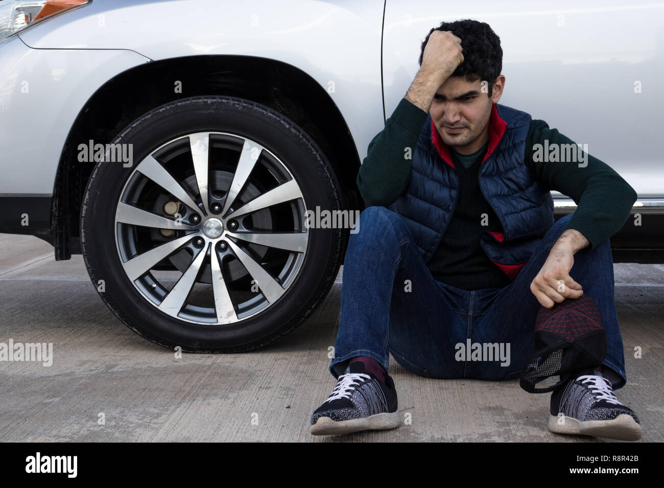 Deprimiert Mann sitzt auf einem Boden lehnte sich auf seinen kaputten Auto. Traurig, wütend und frustriert Person. Notfall. Stockfoto