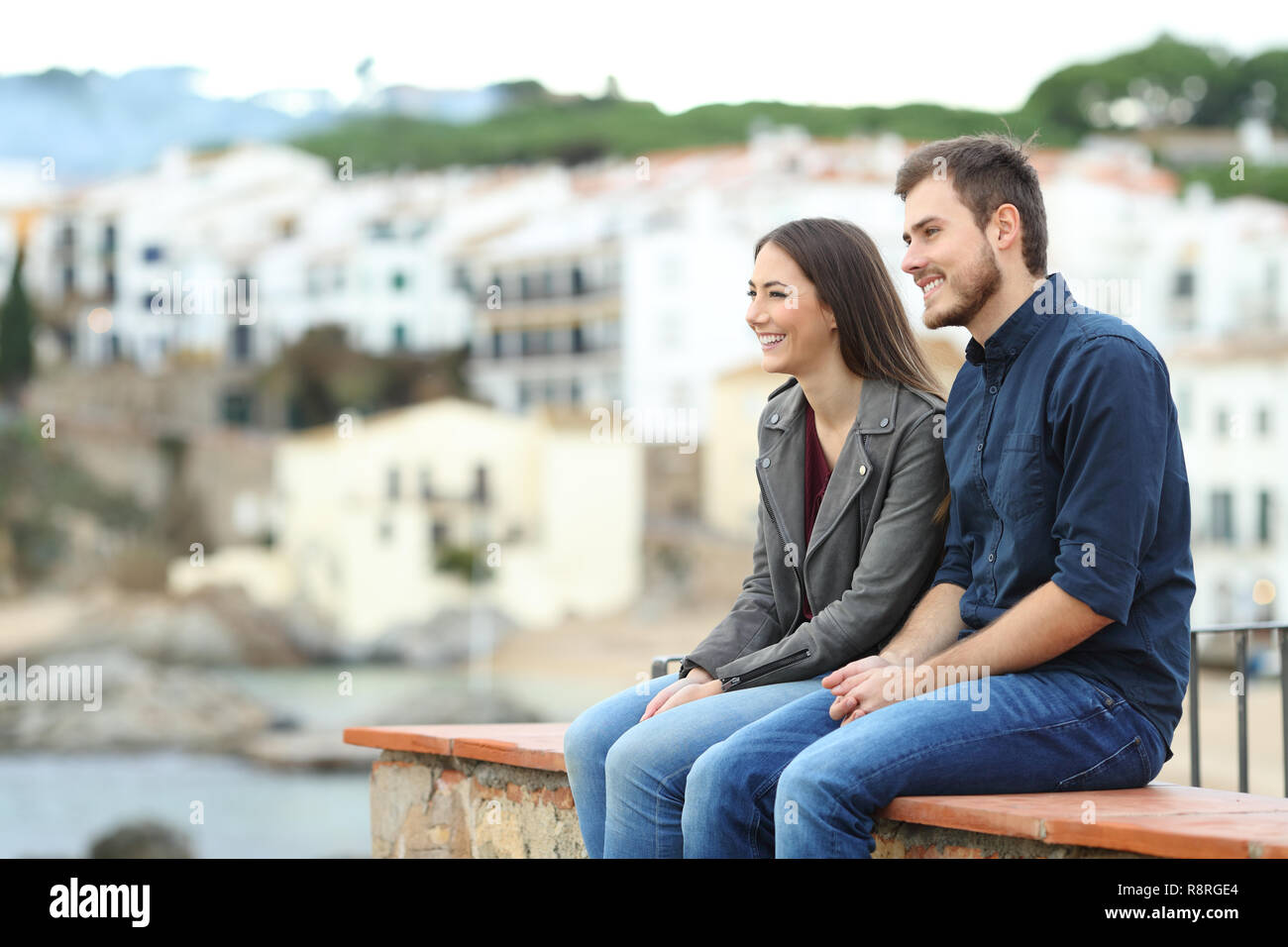 Glückliches Paar oder mit Freunden weg suchen im Urlaub sitzt auf einem Felsvorsprung in einer Küstenstadt Stockfoto