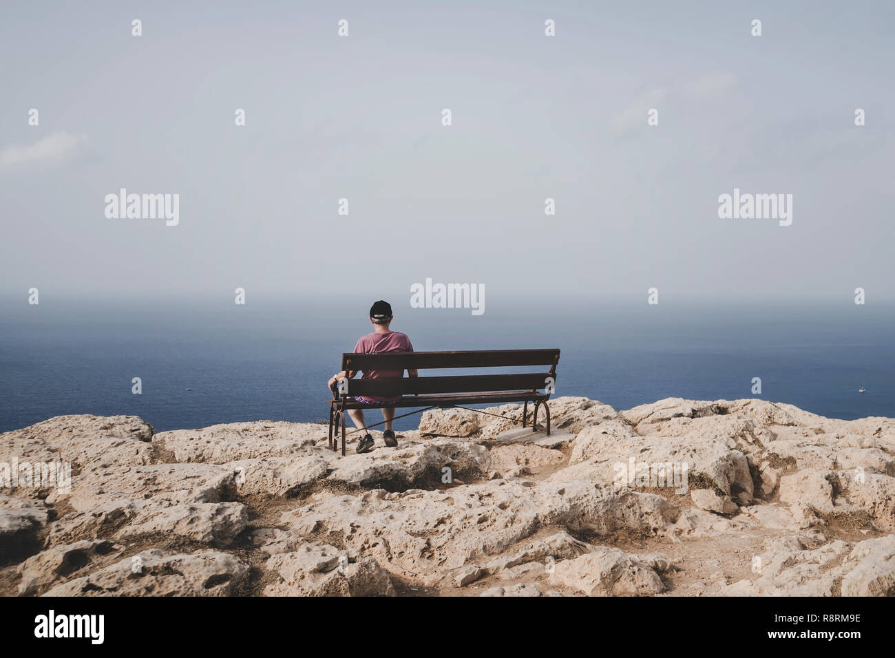 Rentner, die auf einer Bank sitzen und auf das Meer. Alte älterer Mann sitzt alleine auf einer Bank auf einem Felsen und in die Ferne schaut. Konzept der Einsamkeit Stockfoto