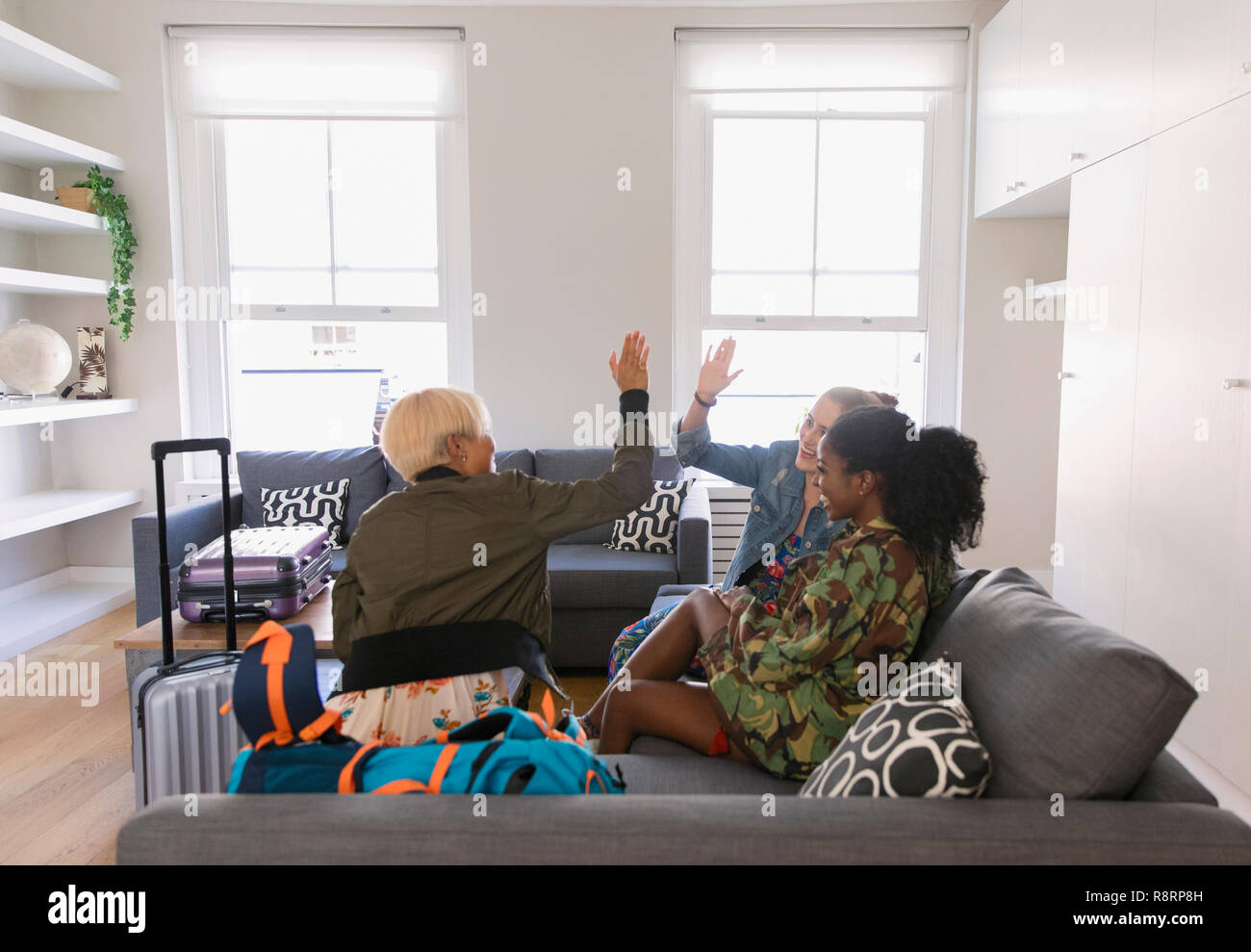 Junge Frauen Freunde mit Koffer high-fiving im Wohnzimmer Stockfoto