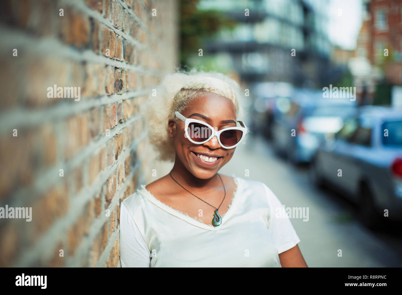 Porträt Lächeln, selbstbewussten jungen Frau in Sonnenbrille auf städtischen Bürgersteig Stockfoto