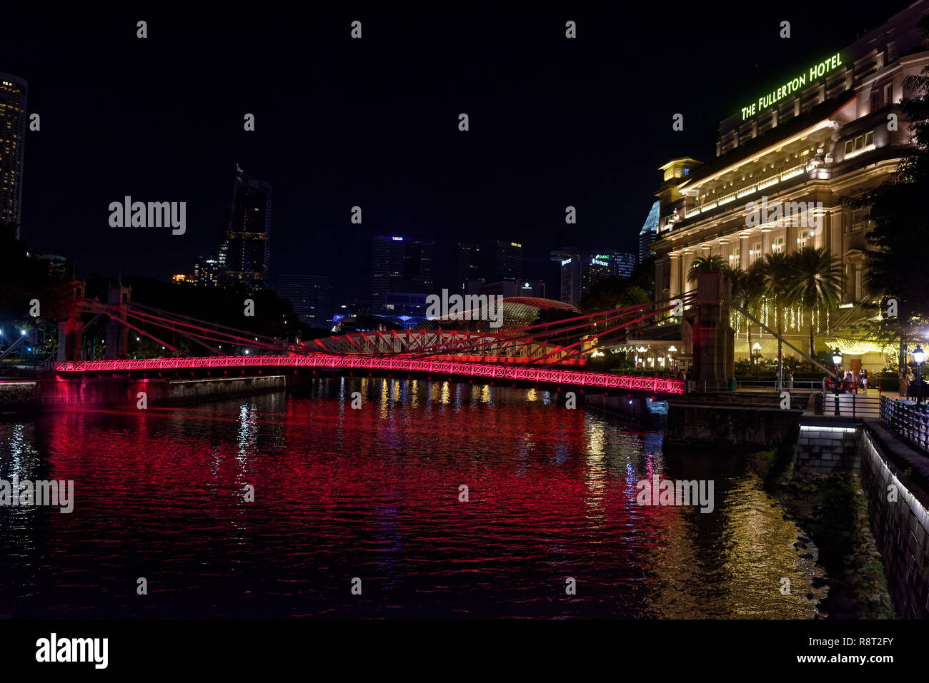 Die cavenaugh Brücke, die einzige Hängebrücke auf dem Singapore River, in rot bei Nacht beleuchtet durch das Fullerton Hotel Stockfoto