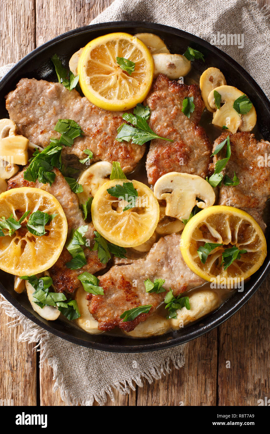 Italienische Kalbfleisch scaloppini mit Pilzen und Zitronen in einer Soße close-up in einer Pfanne auf dem Tisch. Vertikal oben Ansicht von oben Stockfoto