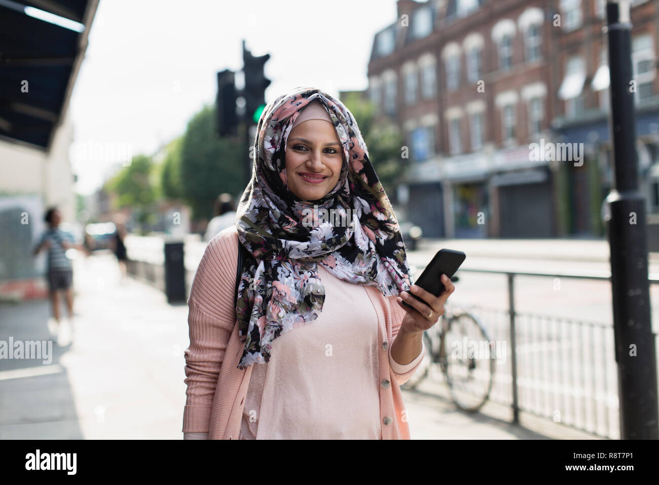 Porträt Lächeln, selbstbewusste Frau mit smart phone tragen Blumen hijab auf städtischen Bürgersteig Stockfoto