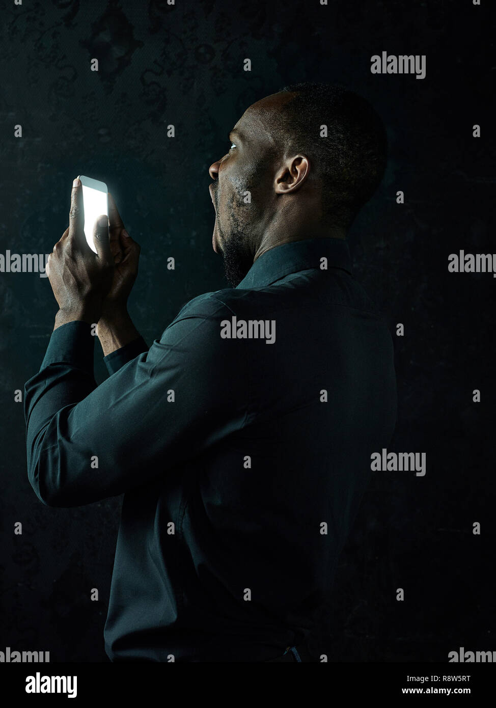 Studio shot Junger schweren schwarzen afrikanischen Mann denken beim Gespräch am Handy gegen Schwarze studio Hintergrund Stockfoto