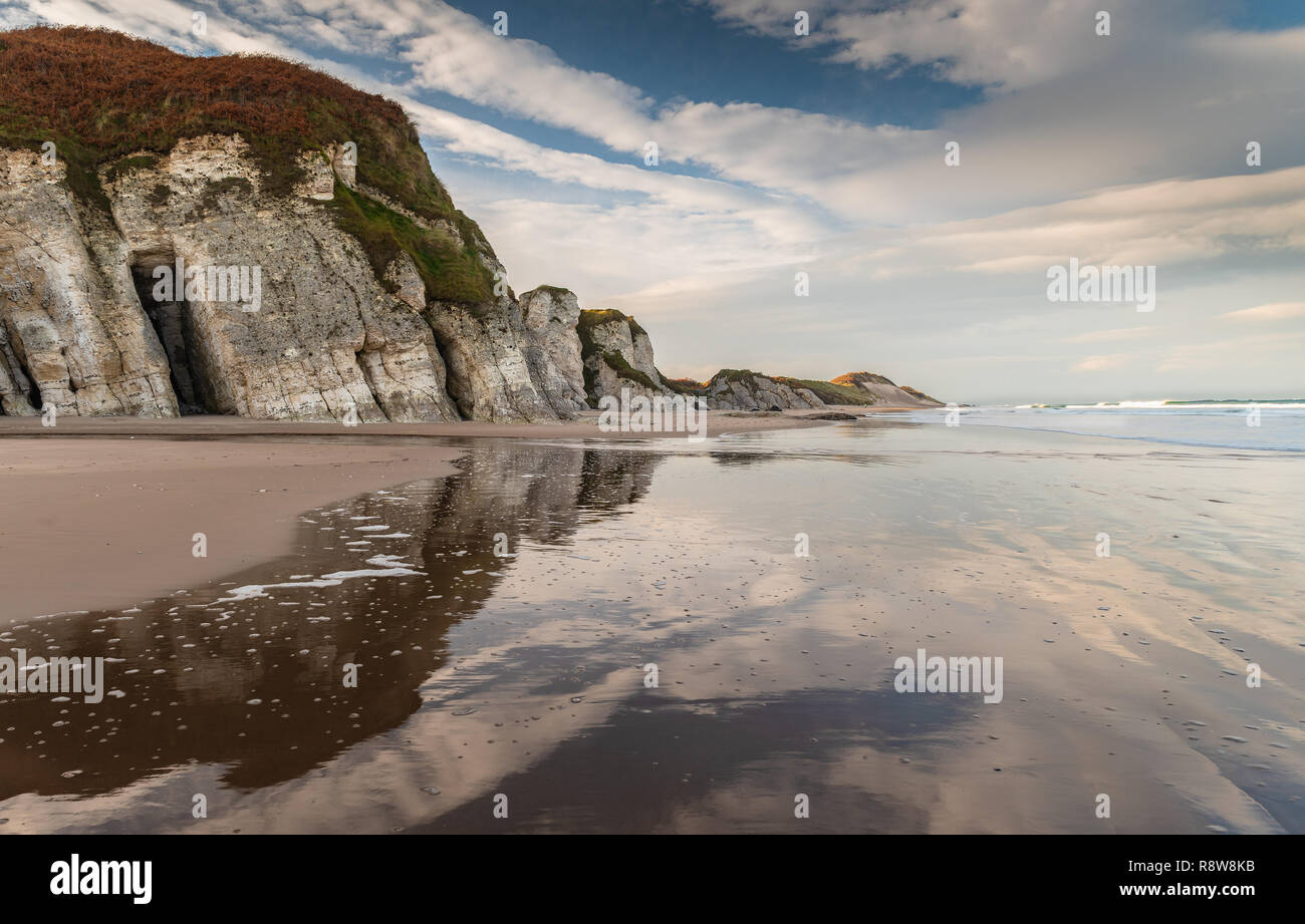 Schöne Strecke von der Küste an der Causeway Coast als whiterock Strand mit Kalksteinfelsen und dramatischen Himmel im Meer widerspiegelt, N Irland Stockfoto