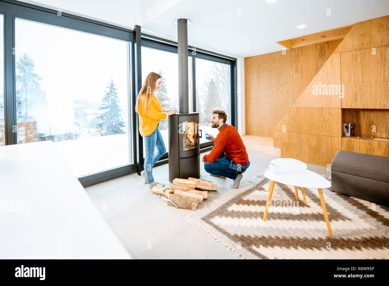 Junges Paar in hellen Pullover aufwärmen in der Nähe der Feuerstelle im modernen Haus in den Bergen im Winter gekleidet Stockfoto