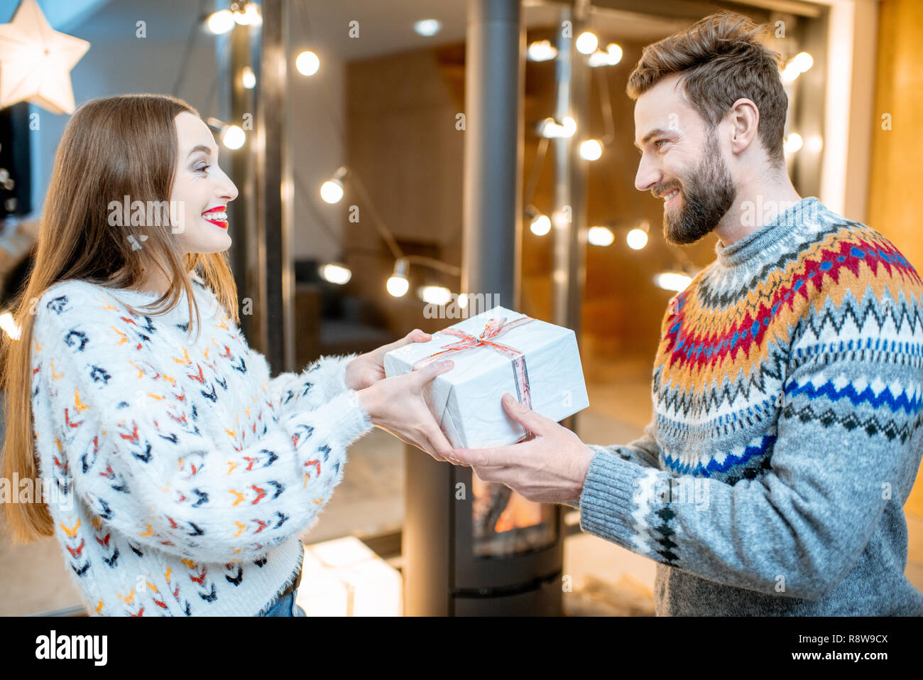 Mann, der ein neues Jahr Geschenk für eine junge Frau feiern Winter Urlaub zu Hause mit Kamin Stockfoto
