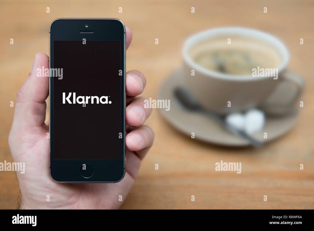 Ein Mann schaut auf seinem iPhone die zeigt die Klarna Logo (nur redaktionelle Nutzung). Stockfoto