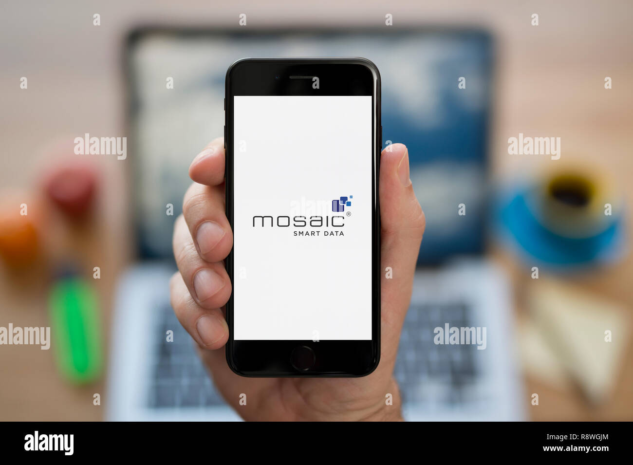 Ein Mann schaut auf seinem iPhone. Das Mosaik Smart Data Logo (nur redaktionelle Nutzung). Stockfoto