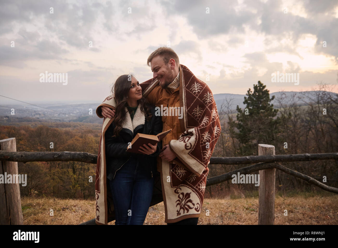 Zwei junge Leute, Paar, ein Buch lesen, im Freien in der Natur, an einander suchen, von Angesicht zu Angesicht. Herbst Kleidung, unter einer Decke. Stockfoto