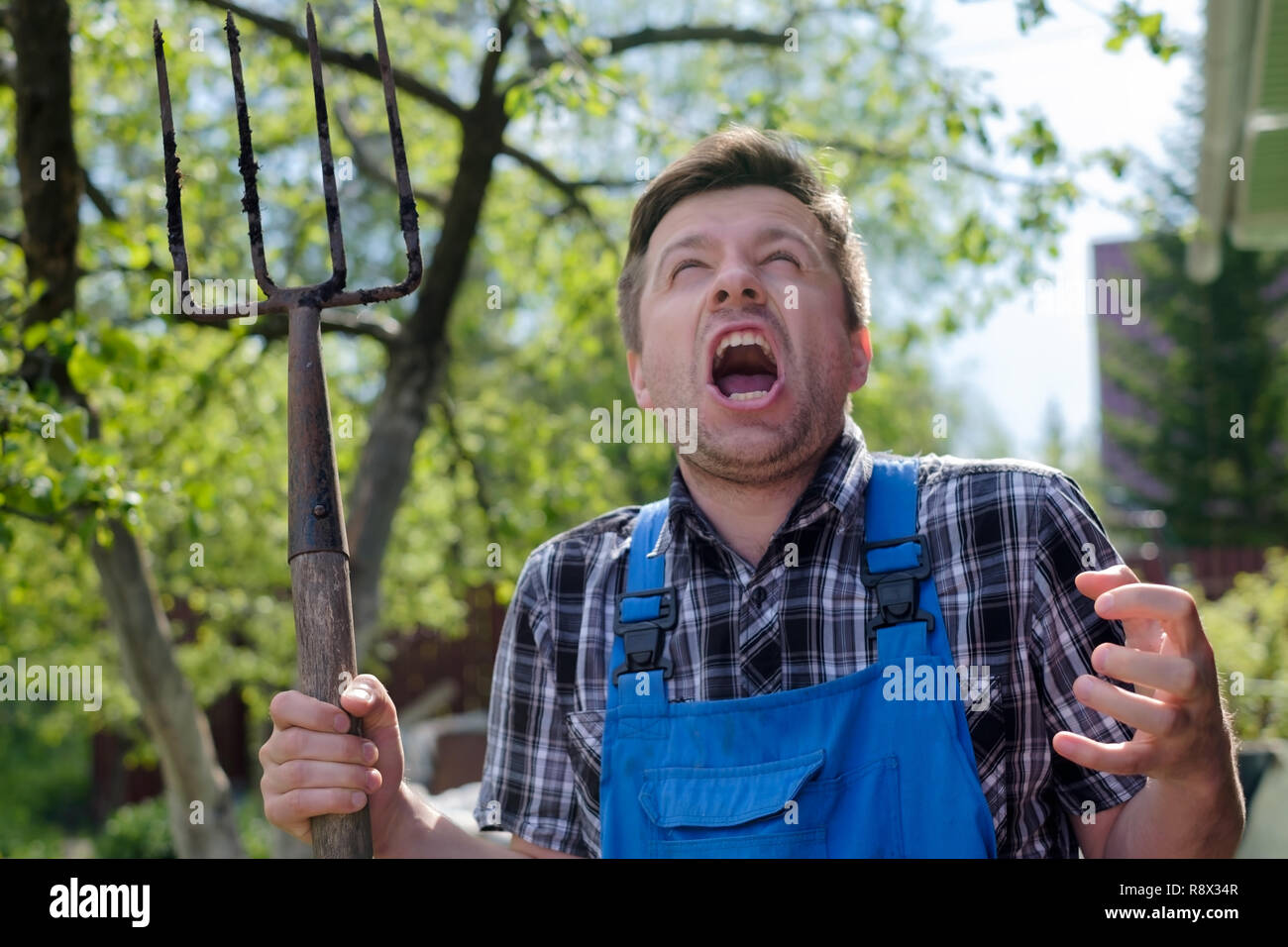 Europäische Mann mit Pitchfork wütend ist, seinen Verstand zu verlieren, stehen im Garten Stockfoto