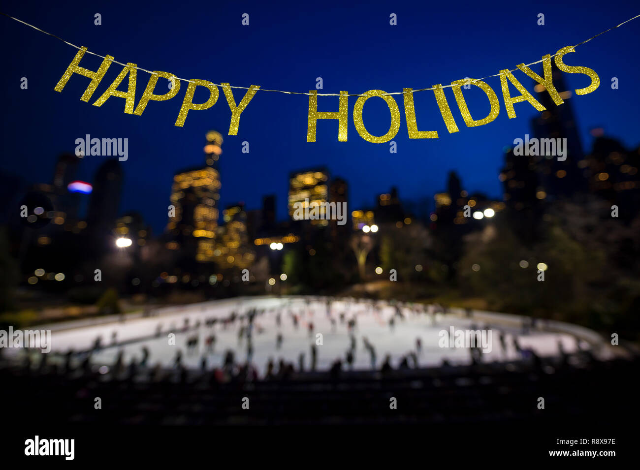 Happy Holidays Nachricht in glänzendem Gold Briefe in den Himmel über einem langen Eisbahn durch die funkelnden Lichter der Stadt umgeben Stockfoto
