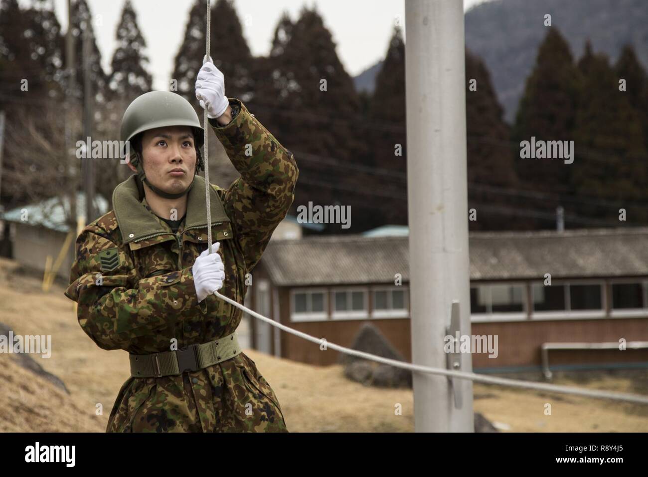 Ein service Mitglied mit der japanischen Boden Verteidigung-kraft die japanische Flagge während der Morgen Farben in der Hijudai Manöver, Japan wirft, 6. März 2017. Us-Marines und Matrosen an der Artillerie relocation Training Programm rechtzeitige und genaue Brände zu stellen militärische beruflichen Spezialgebiet Fähigkeiten, Zug Marines/Matrosen in gemeinsamen Fähigkeiten zu erhalten, und professionelle militärische Ausbildung für das allgemeine Ziel der Verbesserung der Bekämpfung der Betriebsbereitschaft und internationale Beziehungen zu fördern. Stockfoto