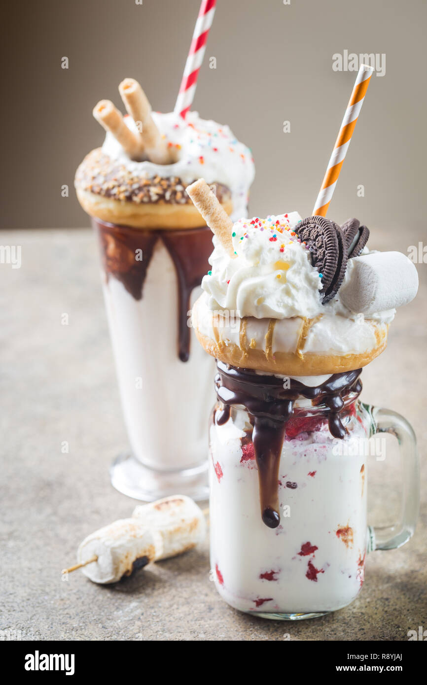 Milch Monster schüttelt oder Freak Schütteln. Big Crazy Milchshake oder Freakshake mit Leckereien und Süßigkeiten mischen. Süßes Getränk Dessert Sammlung in einem Gläser Stockfoto