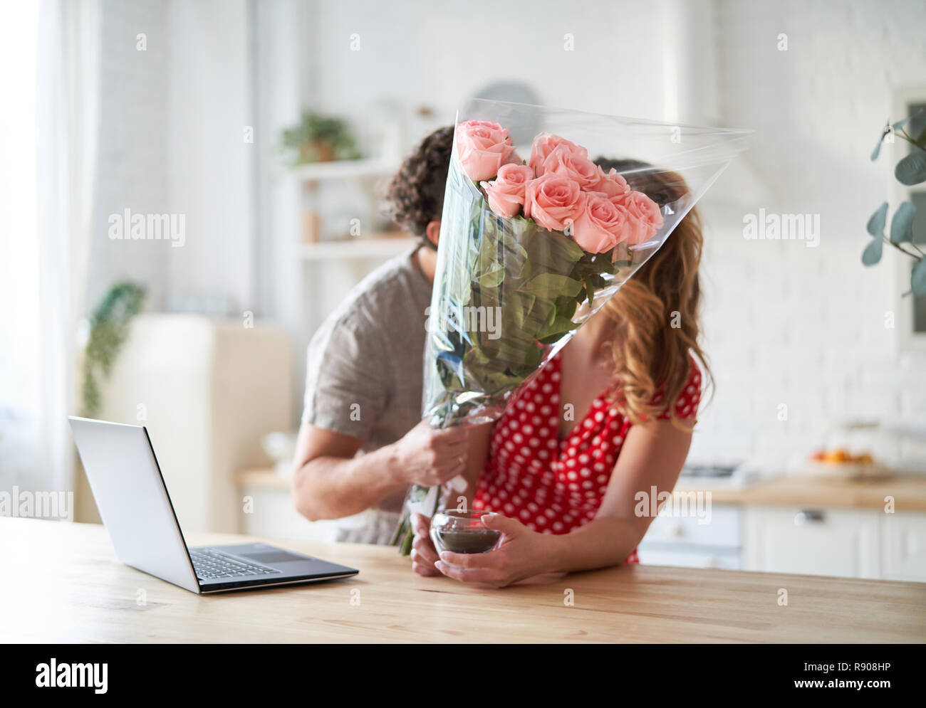 Sommer Urlaub, Liebe, Beziehung - Paar mit Blumenstrauß in der Küche. Laptop auf dem Tisch. Stockfoto