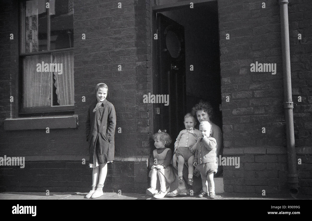 1940, historische, eine Mutter mit ihren Kindern sitzen auf der Türschwelle zu ihrer städtischen viktorianischen Reihenhaus, England, UK. Stockfoto