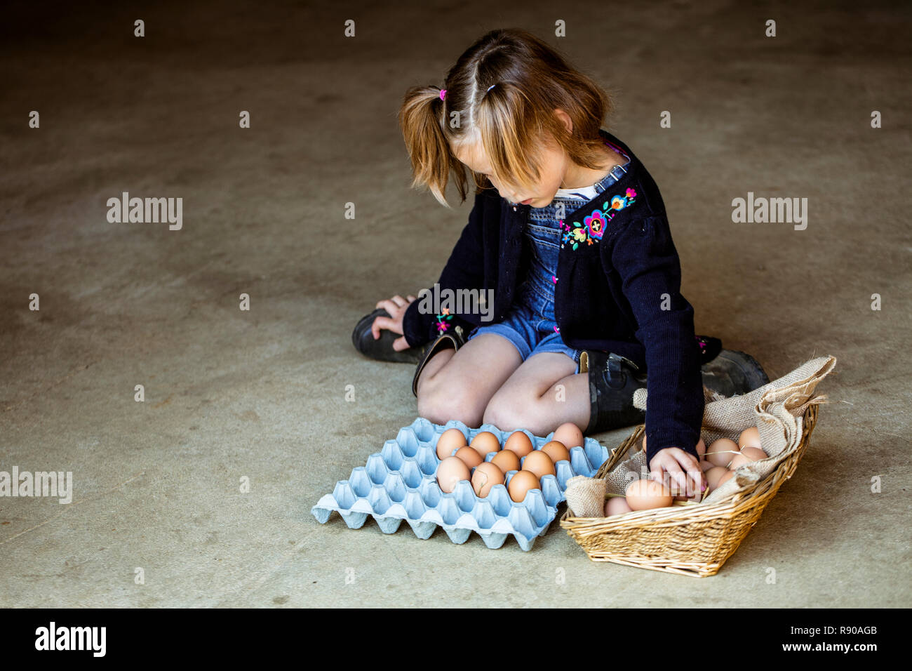 Mädchen kniend auf dem Boden, legen Eier in einen Korb. Stockfoto