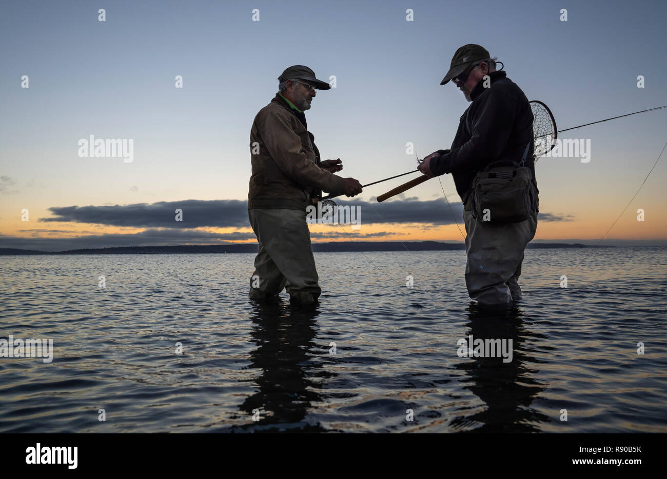 Ein männlicher Fliegenfischer Uhren sein Guide arbeiten Sie ein neues Fliegenfischen auf Lachs oder Forelle auf ein Salz Wasser Strand in Fort Flagler State Park zu versuchen in Nord Stockfoto