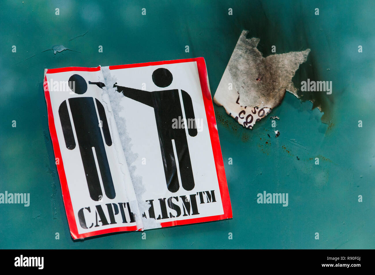 Teilweise Aufkleber mit Piktogramm zeigt eine Person eine Pistole an den Kopf einer anderen Person, zerrissen, Text lautet: 'Kapitalismus', Stockfoto