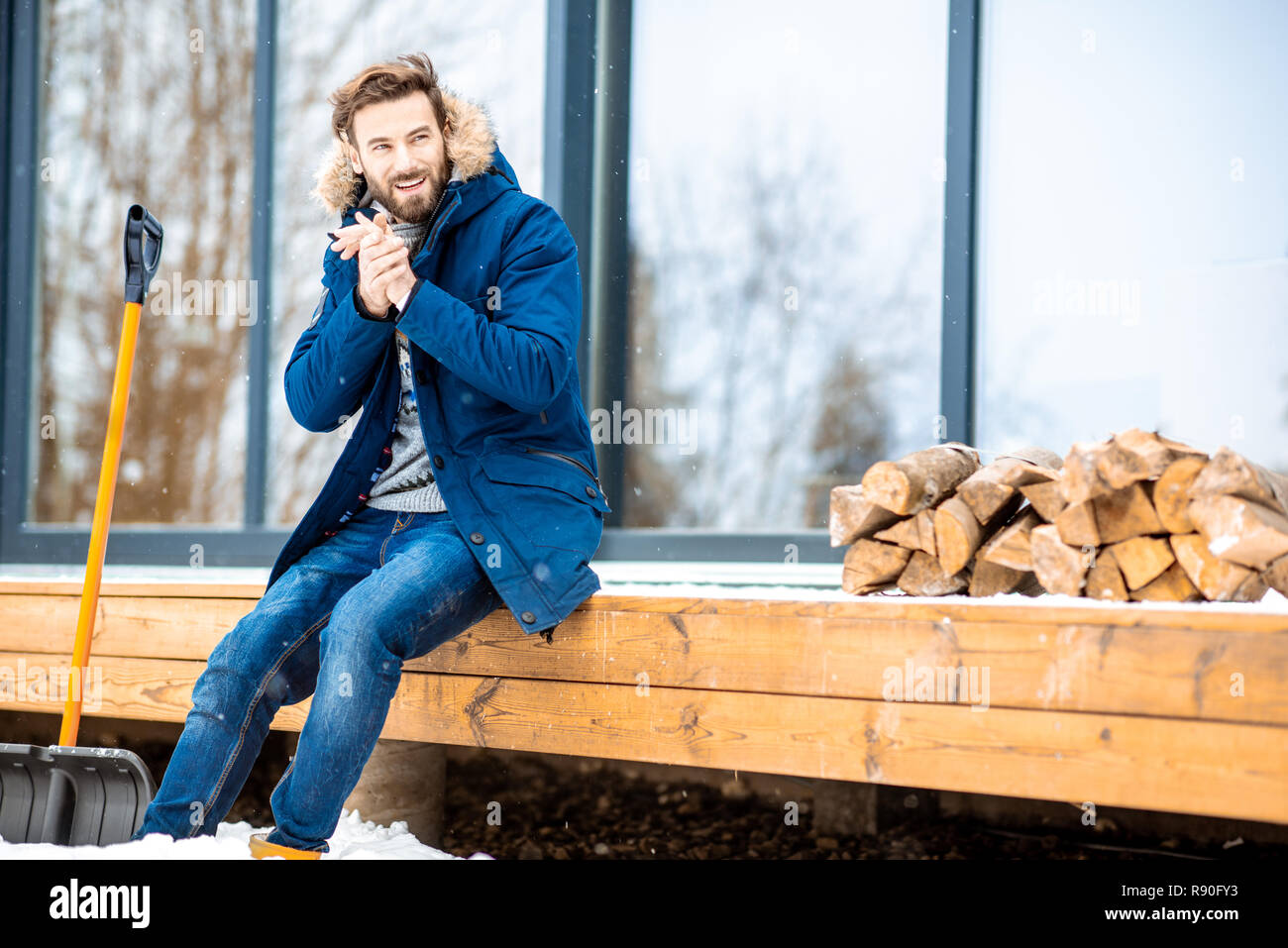 Porträt eines gutaussehenden Mann im Winter Kleidung füllen Kalten sitzen auf der Terrasse des modernen Haus Stockfoto