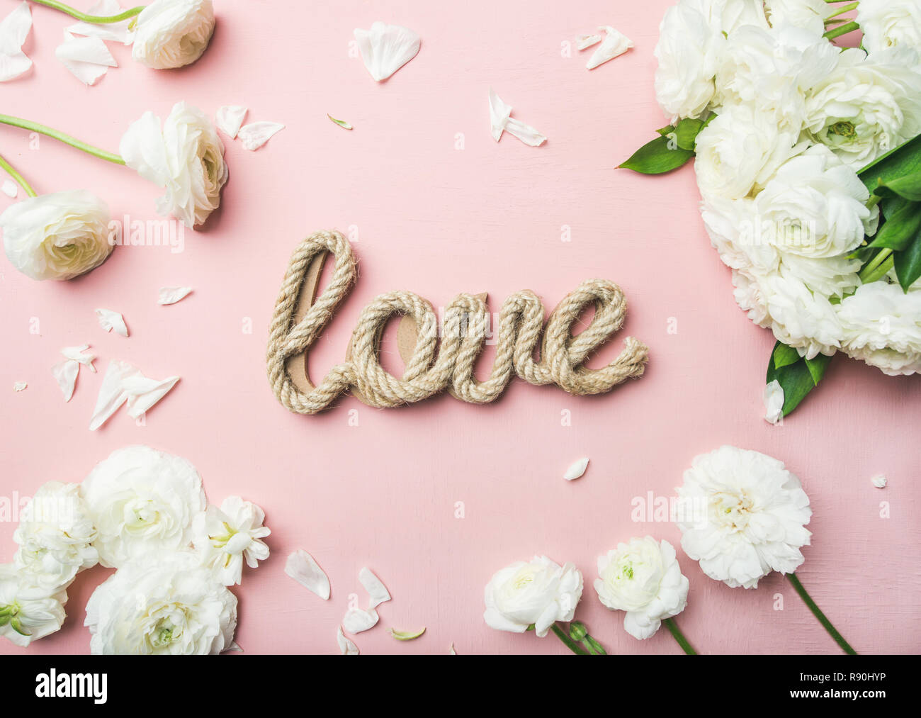 Saint Valentines Tag Hintergrund. Flachbild-lay der Weißen ranunkeln Blumen und Wort Liebe über leicht rosa unterlegt, Ansicht von oben. Grußkarte oder Hochzeit inv Stockfoto