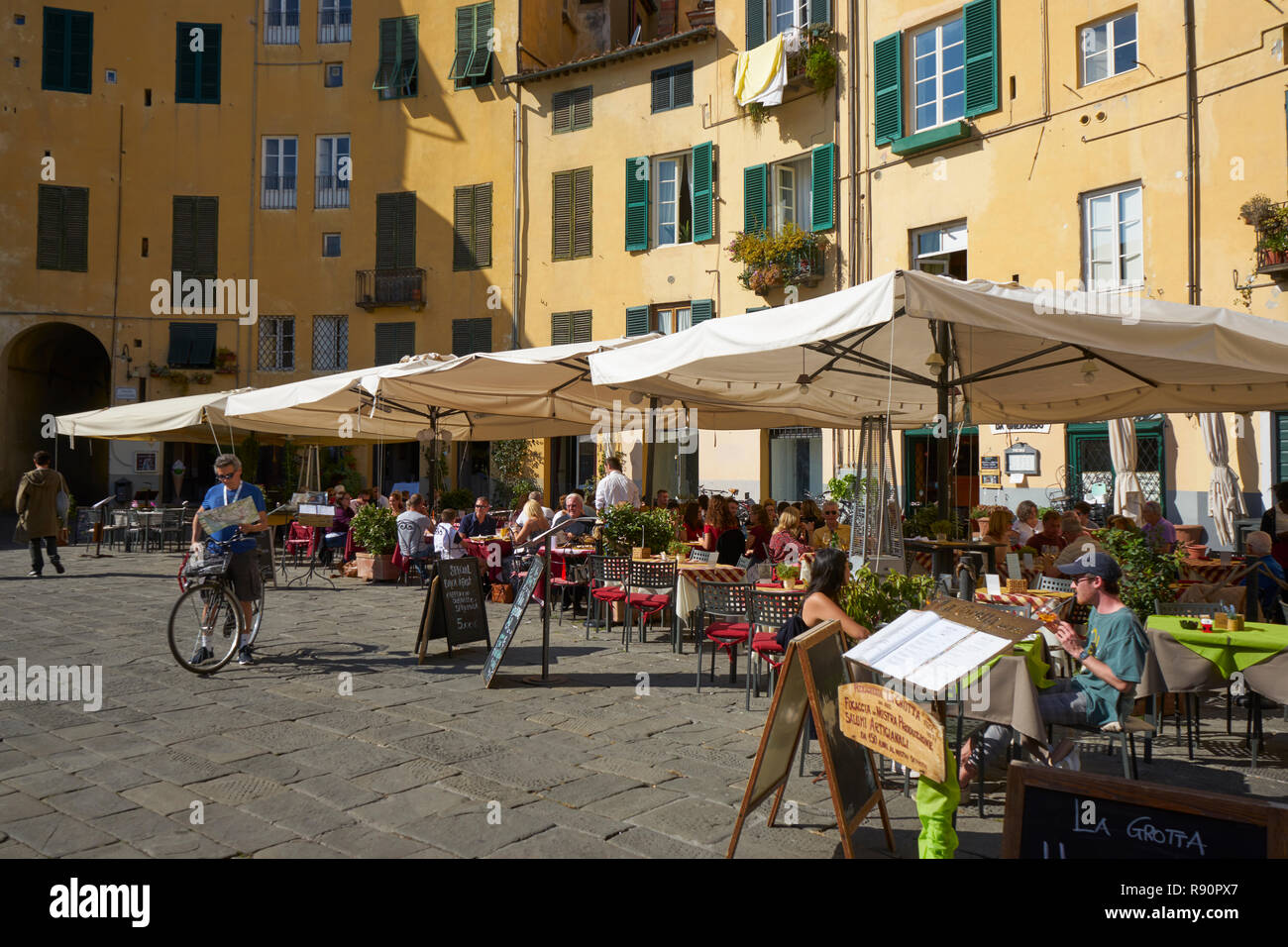 Lucca, Italien: Restaurants und Cafés an der Piazza Anfiteatro, einer alten römischen Amphitheater, Mann auf dem Fahrrad Studium der Karte Stockfoto